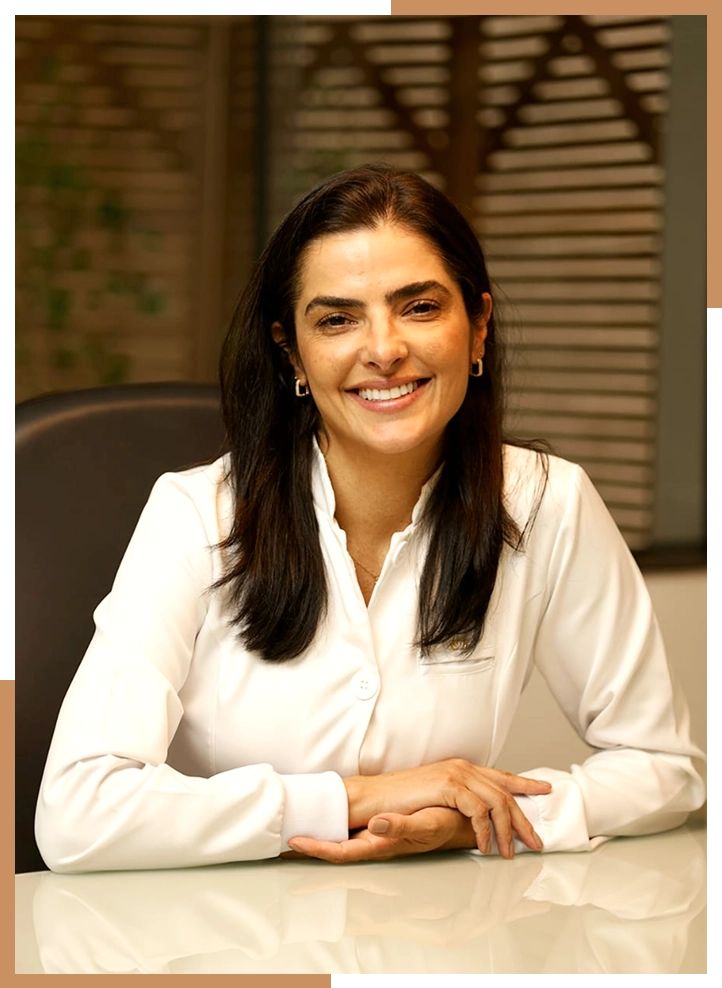 Dra. Lidiana sorrindo em sua mesa de atendimento, de jaleco branco